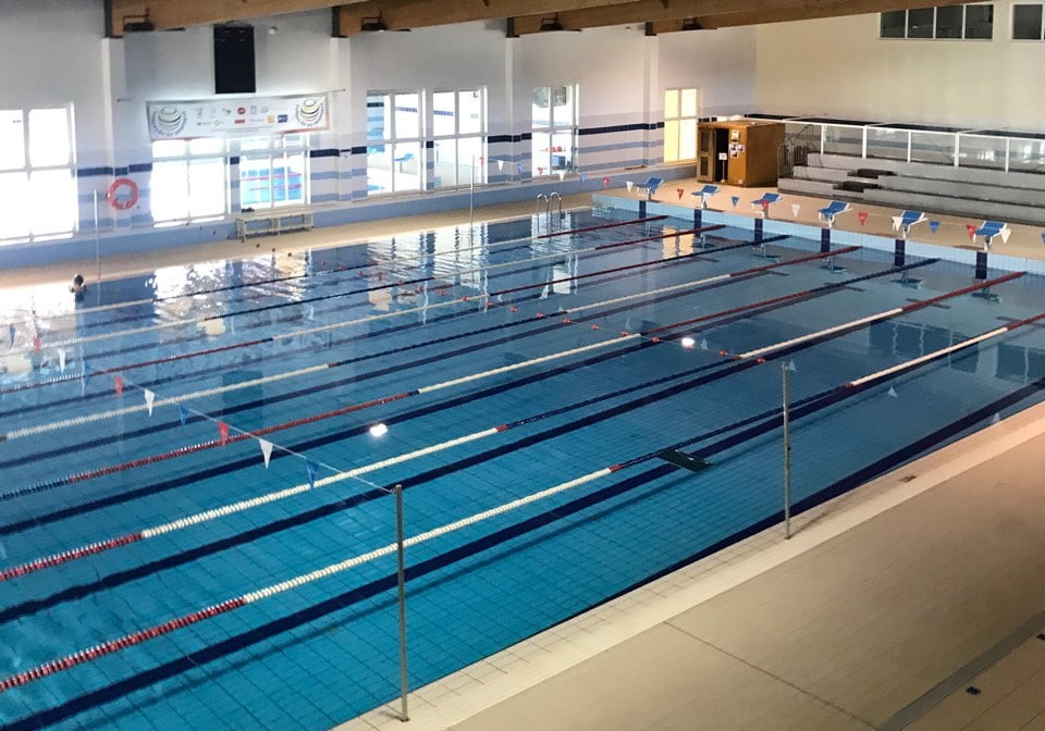 Weitwinkelansicht eines Hallenbads mit Schwimmleinen und Zuschauertribüne.