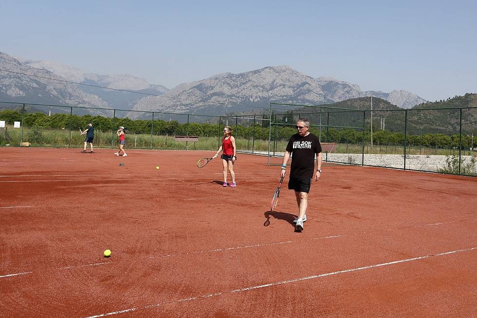 Sandplatz mit Spielern und Bällen, Berge hinter dem Zaun.