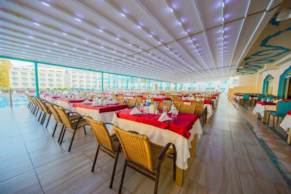 Überdachte Restaurantterrasse mit langen Tischreihen und hellen Sitzbereichen.