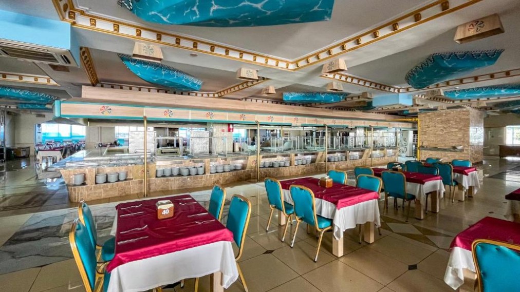 Innenbereich des Buffetrestaurants mit gedeckten Tischen, türkisfarbenen Stühlen und Ausgabetheken.