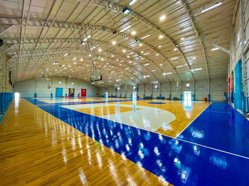 Weitwinkelansicht eines Hallen-Basketballfelds unter Bogendach mit heller Beleuchtung.