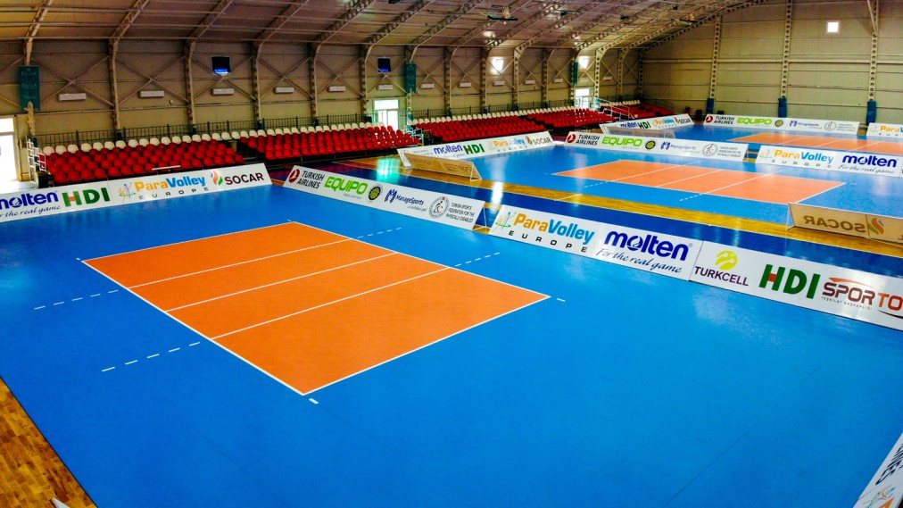 Indoor-Volleyballfeld mit Sitzreihen und markierten Spielflächen.