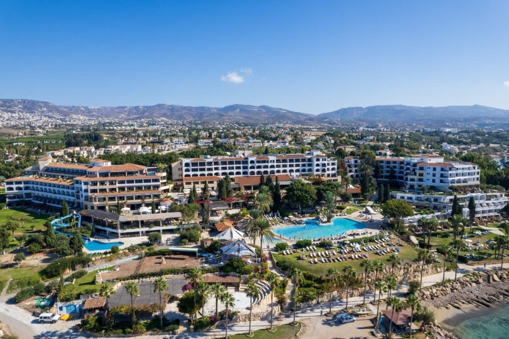 Panoramablick auf Resortgebäude, Pools und Küstenbereich mit Bergen in der Ferne