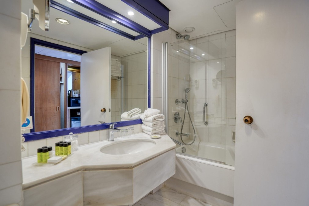 Badezimmer mit weißen Fliesen, Badewanne und Ablage mit Pflegeprodukten und gefalteten Handtüchern