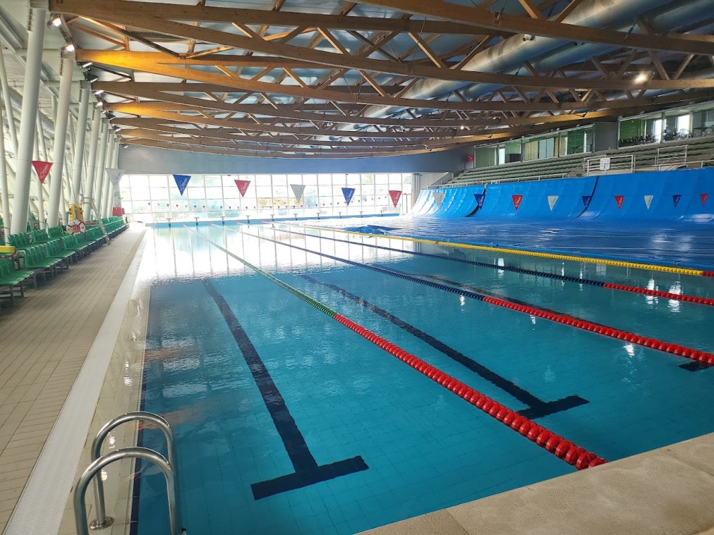 50-Meter-Hallenbecken mit Leinen, einer Einstiegsleiter und überdachtem Sitzbereich.