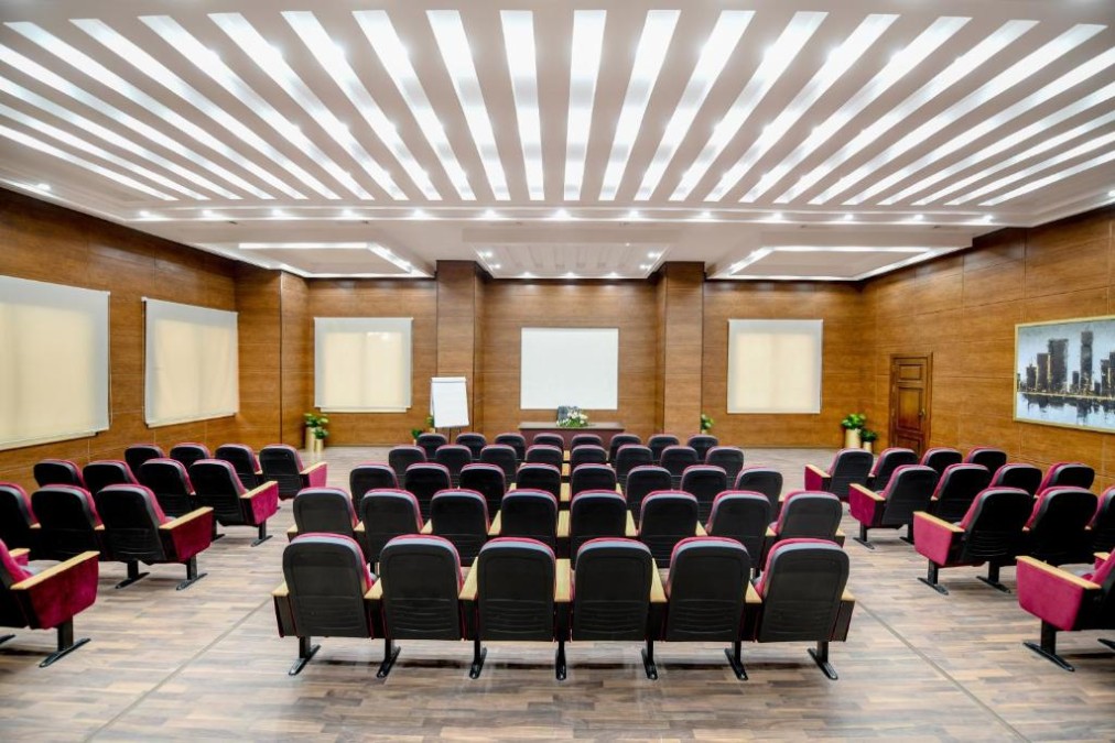 Konferenzsaal mit Reihen roter Stühle, die auf eine Projektionsleinwand ausgerichtet sind