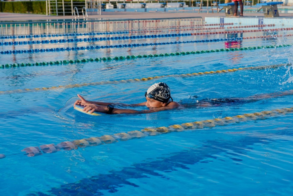 Schwimmer mit Badekappe trainiert mit Schwimmbrett im olympischen Freibad
