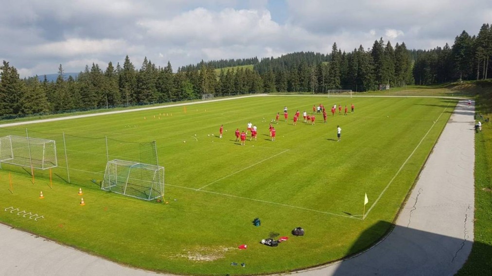 Fußballtraining im Freien auf einem Rasenplatz mit Hütchen, kleinen Toren und umlaufender Laufbahn.