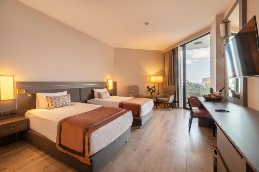 Zweibettzimmer mit zwei Einzelbetten, Nachttischbeleuchtung, Schreibtisch und Balkonzugang mit Meerblick.