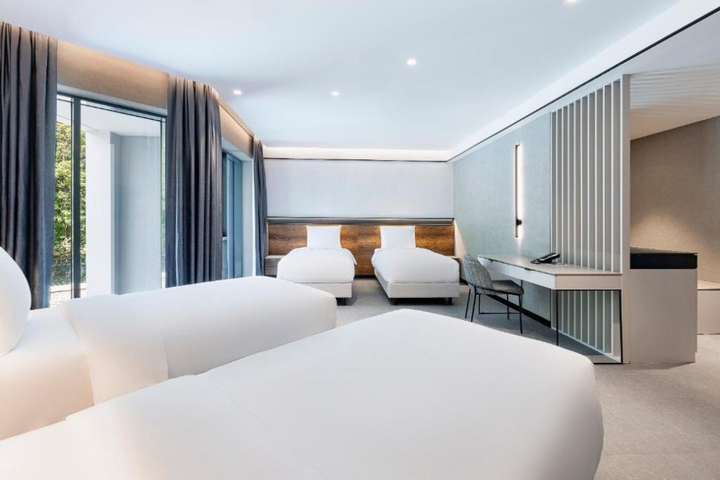 Großes, modernes Gästezimmer mit mehreren Betten, bodentiefen Fenstern und Arbeitsbereich.