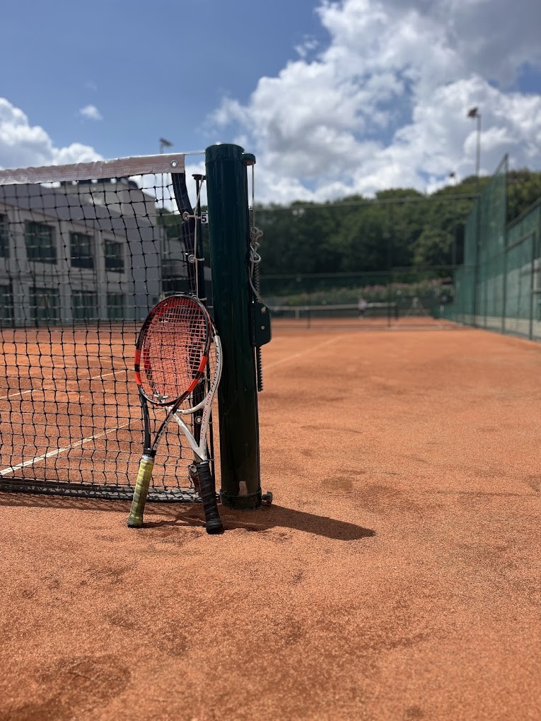 Tennisnetz auf einem Sandplatz mit zwei Schlägern am Pfosten.