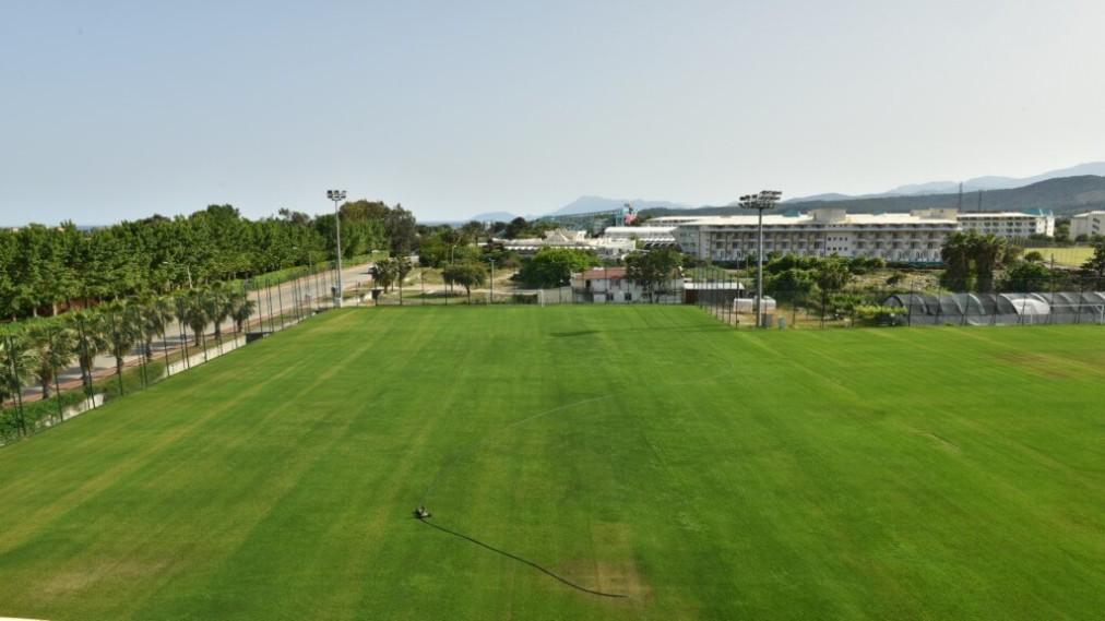 Rasen-Fußballplatz in voller Größe mit Flutlichtmasten nahe der Hotelanlage, Blick von der Grundlinie.