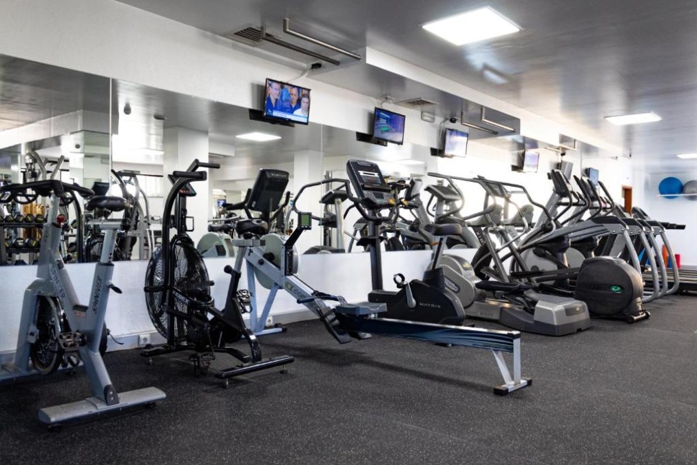 Fitnessraum mit Cardiogeräten, Rudergerät und Spiegelwand.