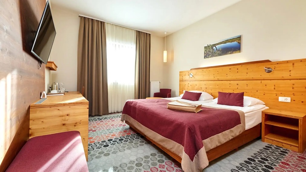 Helles Doppelzimmer mit Schreibtisch, TV und Sitzbereich am Fenster.
