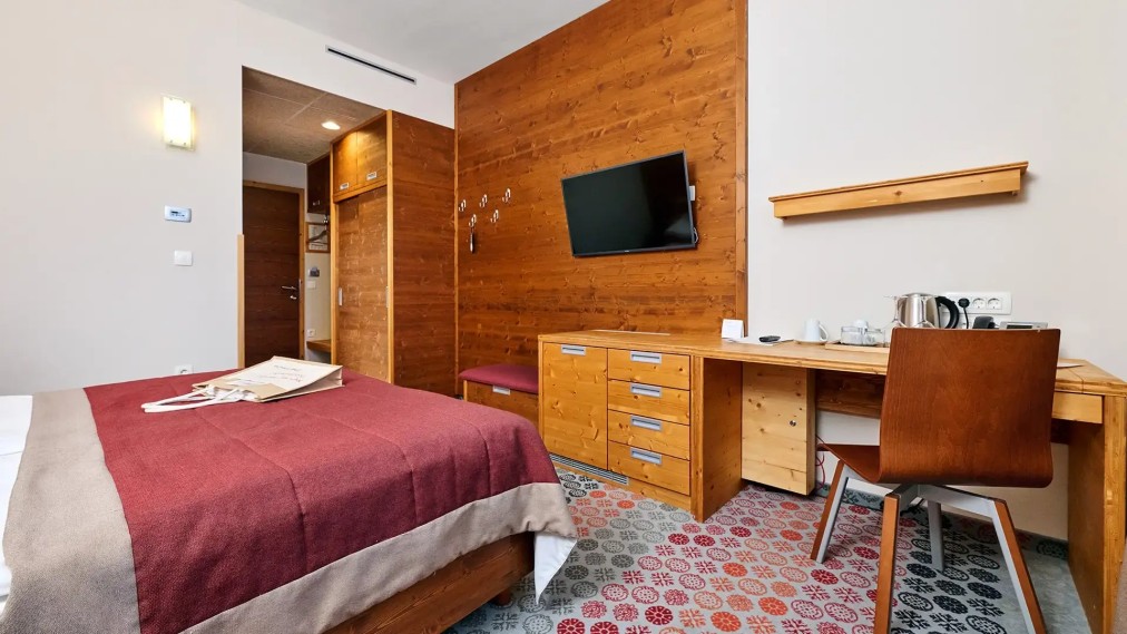 Gästezimmer mit Holzschreibtisch, Wand-TV und Stauraummöbeln.