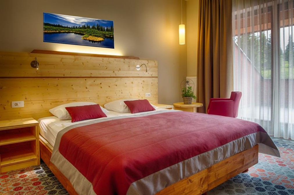 Doppelzimmer mit Holzmöbeln, roter Bettwäsche und großem Fenster.