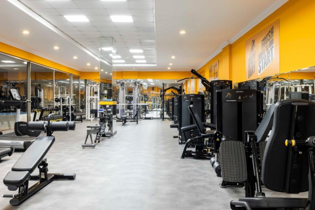 Weitwinkelansicht des Fitnessraums mit Bänken, Gewichten und Kraftgeräten.