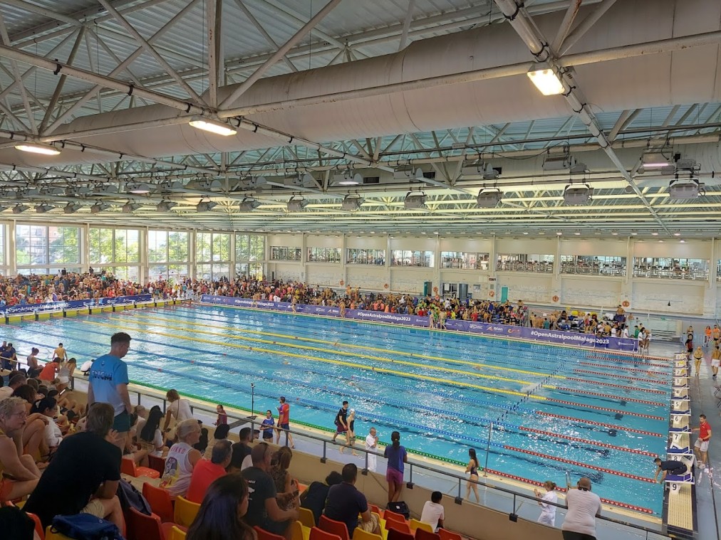Wettkampfbecken in der Halle während einer Veranstaltung, über Reihen von Tribünensitzen hinweg.