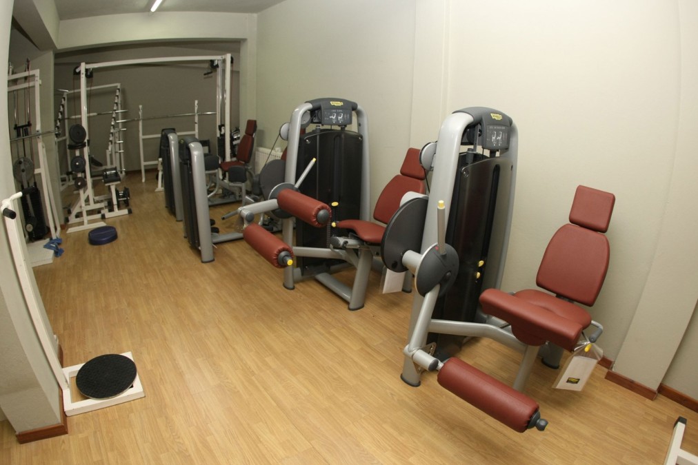 Kompakter Fitnessraum mit Kraftgeräten, Bänken und Freihantelausstattung.