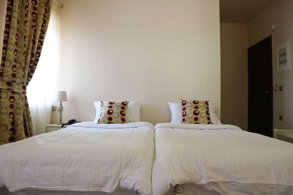 Zweibettzimmer mit zwei Betten, gemusterten Kissen und hellem Fenster.