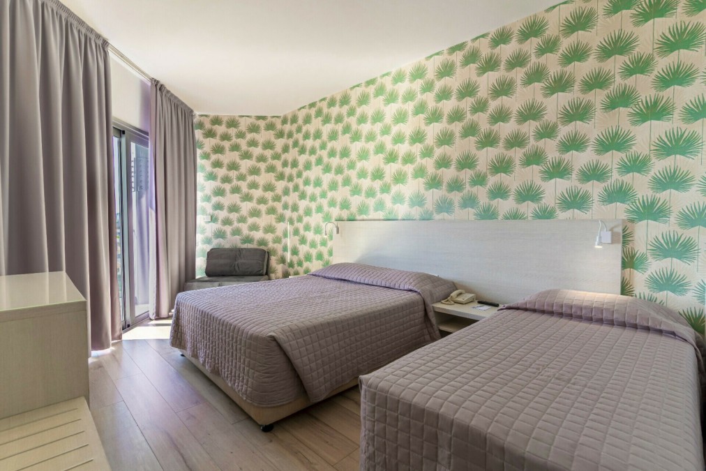 Hotelzimmer mit zwei Doppelbetten, grüner gemusterter Tapete und Sessel