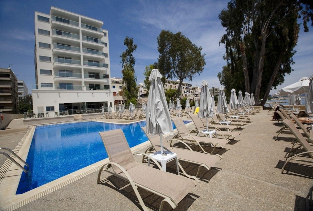 Außenpoolbereich mit Sonnenliegen vor einem modernen mehrstöckigen Hotel