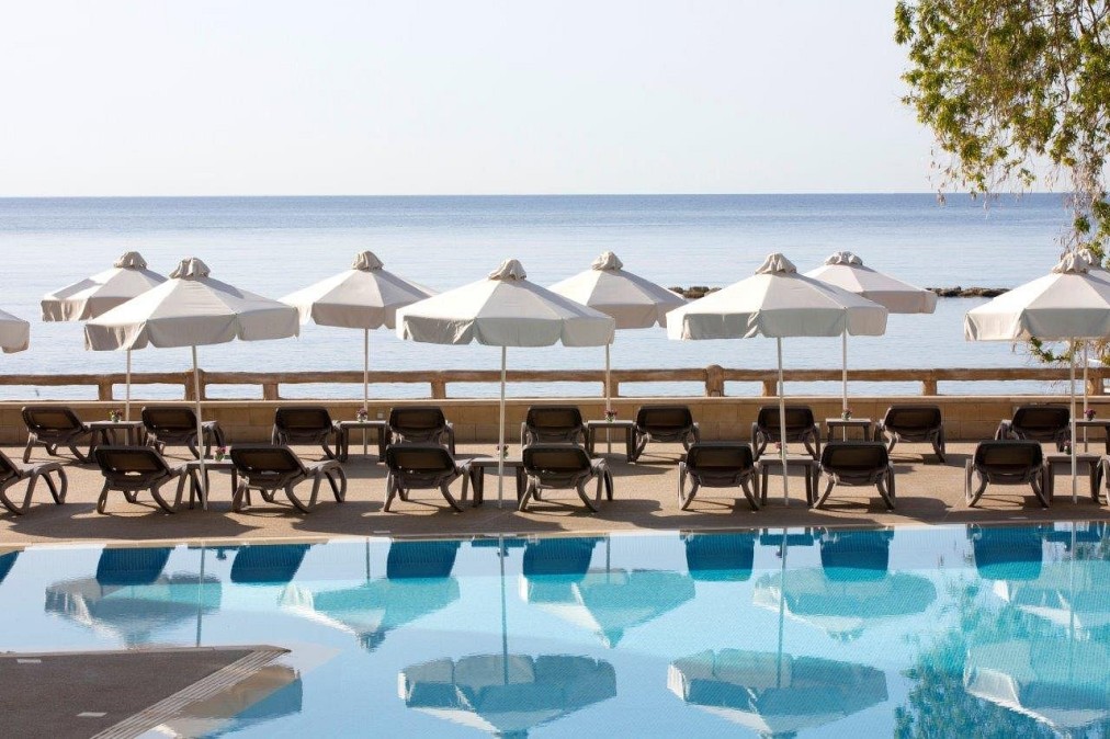 Poolblick mit Reihen von Sonnenliegen und weißen Sonnenschirmen mit Blick auf das ruhige blaue Meer