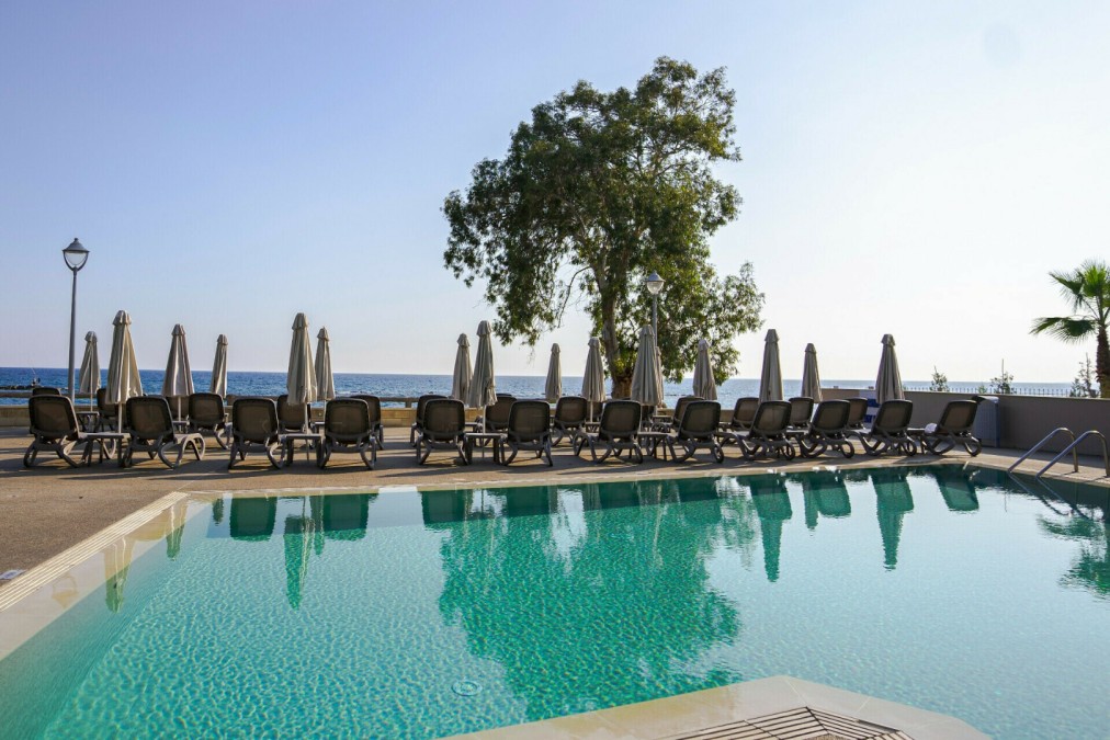 Außenpool mit Reihen von Sonnenliegen und Sonnenschirmen mit Blick auf das Meer