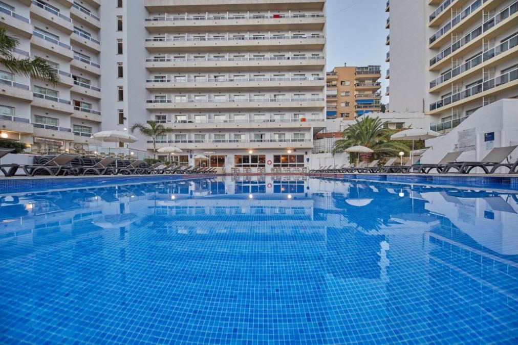 Großer Außenpool mit umliegenden Sonnenliegen und Hotelgebäuden.