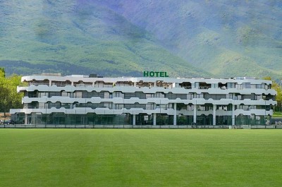 Hotelgebäude mit Blick auf einen grünen Fußballplatz und Berge im Hintergrund, Unterkunft für ein Sporttrainingslager