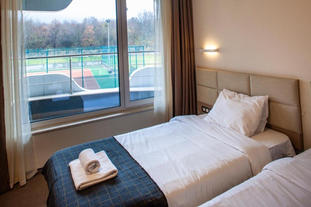 Hotelzimmer mit zwei Einzelbetten und Balkonblick auf Sportplätze, Unterkunft für Athleten im Trainingslager