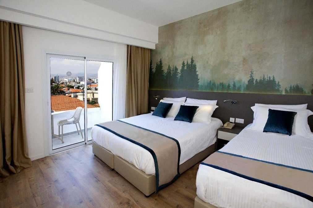 Zimmer mit einem Doppelbett, einem Einzelbett, Wald-Wandbild und Balkontüren mit Blick auf die Stadt.