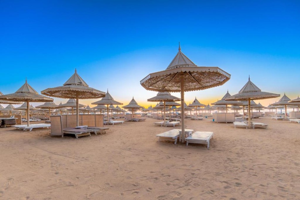 Sandstrand mit weißen Liegen und Sonnenschirmen unter klarem blauem Himmel