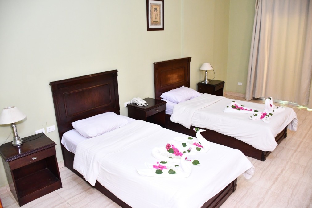 Hotelzimmer mit zwei Einzelbetten, Holzmöbeln und Handtuchschwänen, die mit Blumen dekoriert sind