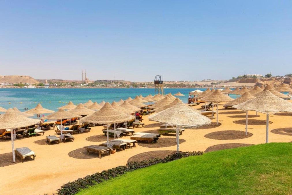 Sandstrand mit Strohschirmen, Sonnenliegen und klarem blauem Meer unter sonnigem Himmel