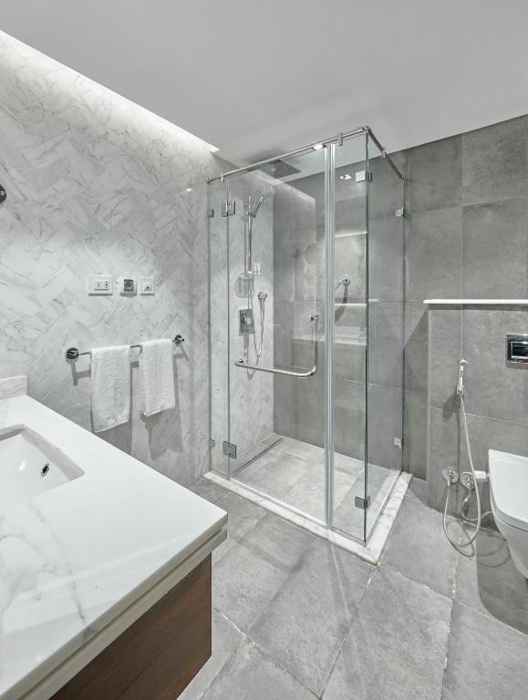 Modernes Badezimmer mit begehbarer Glasdusche, grauen Fliesen, Waschtisch, Toilette und weißen Handtüchern