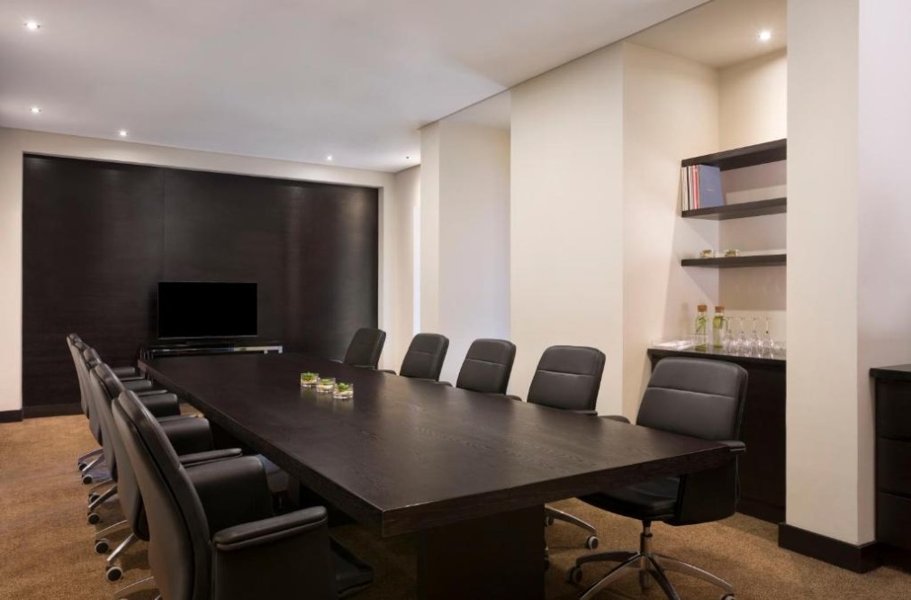 Meetingraum im Boardroom-Stil mit langem Tisch, Ledersesseln und TV-Bildschirm.