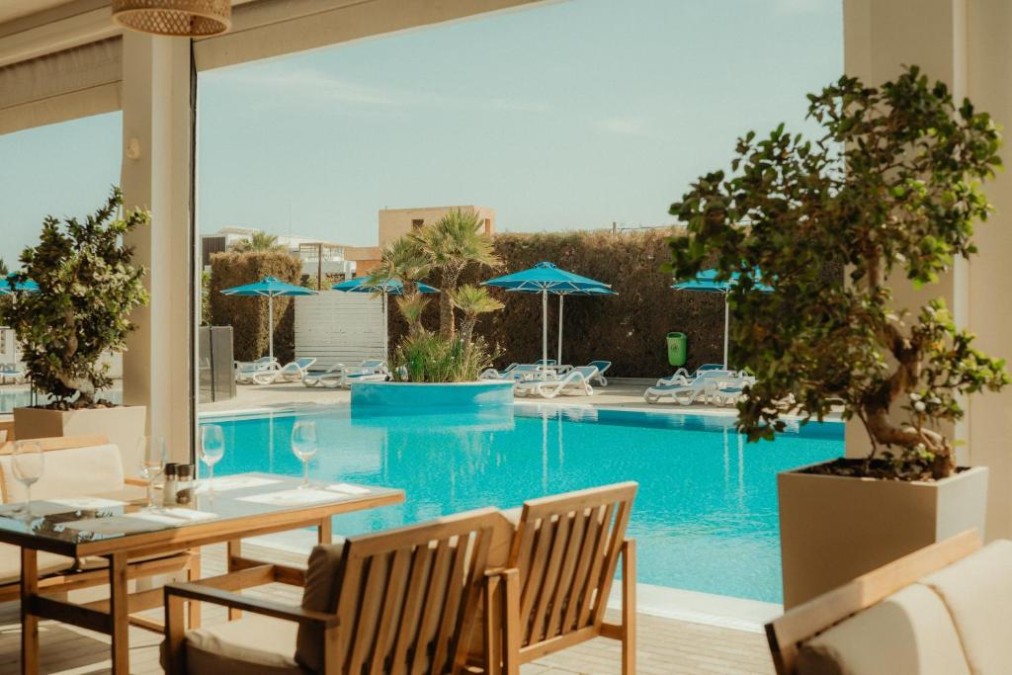 Poolseitige Terrasse mit Tischen, Pflanzen und Blick über den Außenpool.