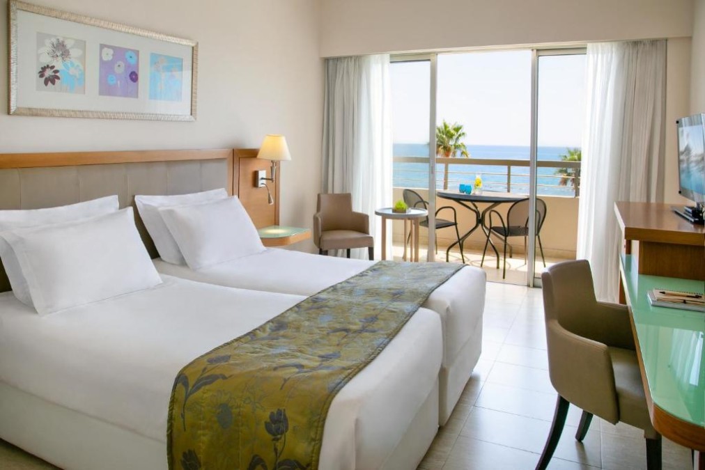 Gästezimmer mit Meerblick-Balkon, zwei Betten, Schreibtisch und Sessel.