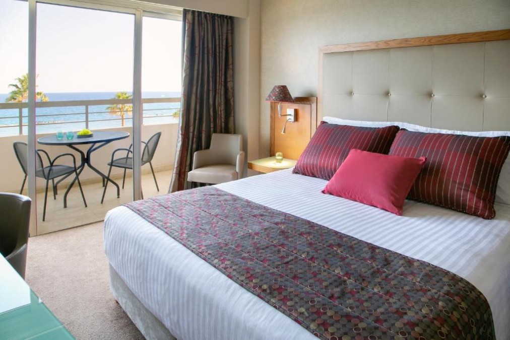 Gästezimmer mit Meerblick-Balkon, Doppelbett und Sitzecke.