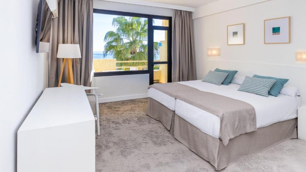 Gästezimmer mit zwei Betten, Meerblick-Fenster und Palmen draußen.