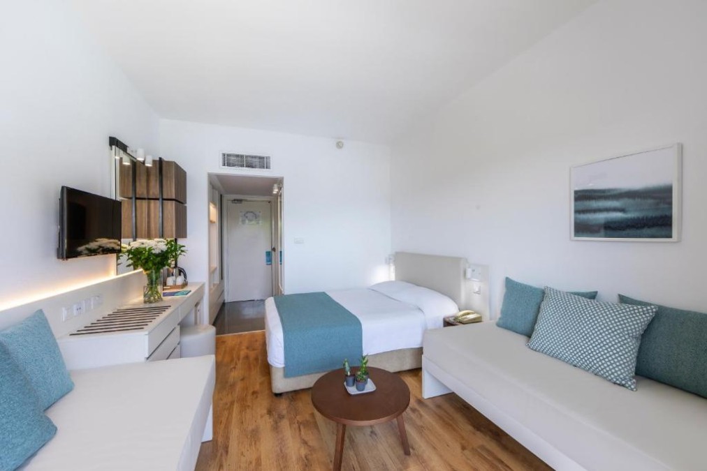 Helles Gästezimmer mit Bett, Sofa, Rundtisch und Schreibtischbereich.