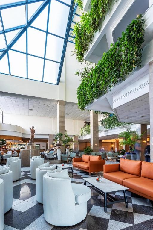 Hotelatrium mit Sitzbereichen, Pflanzen und Glasdach.