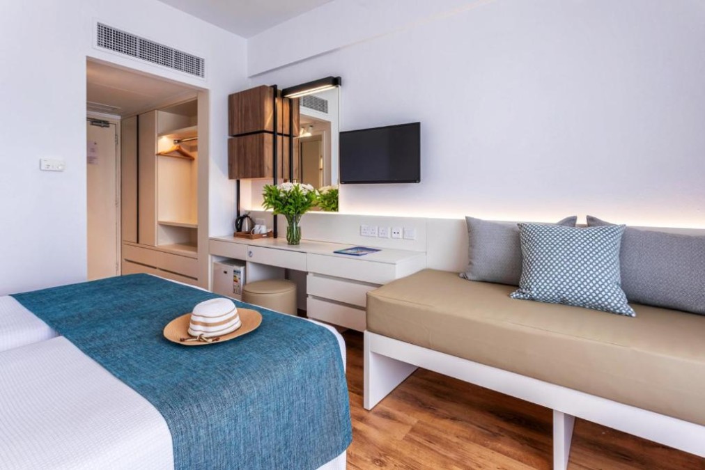 Modernes Gästezimmer mit Bett, Sofa, Schreibtisch, TV und offenem Kleiderschrank.
