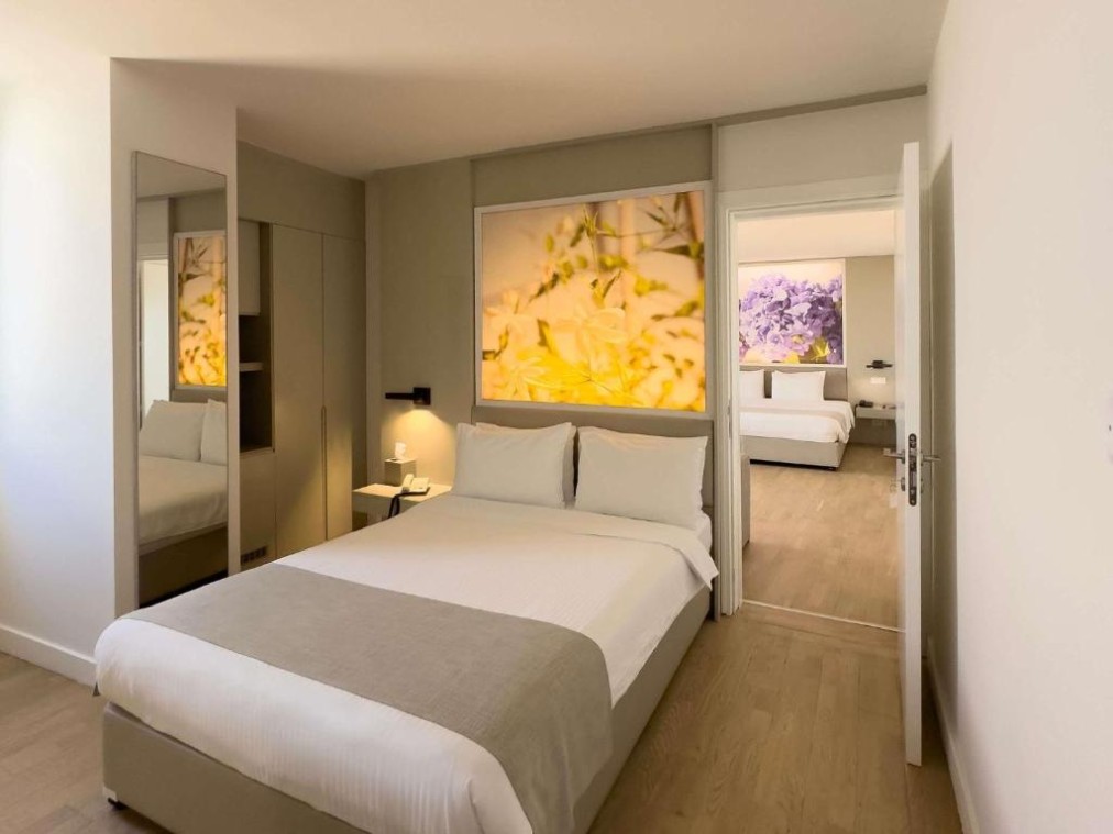 Schlafzimmer mit Doppelbett und Kleiderschrank, verbunden mit einem zweiten Zimmer im Hintergrund.