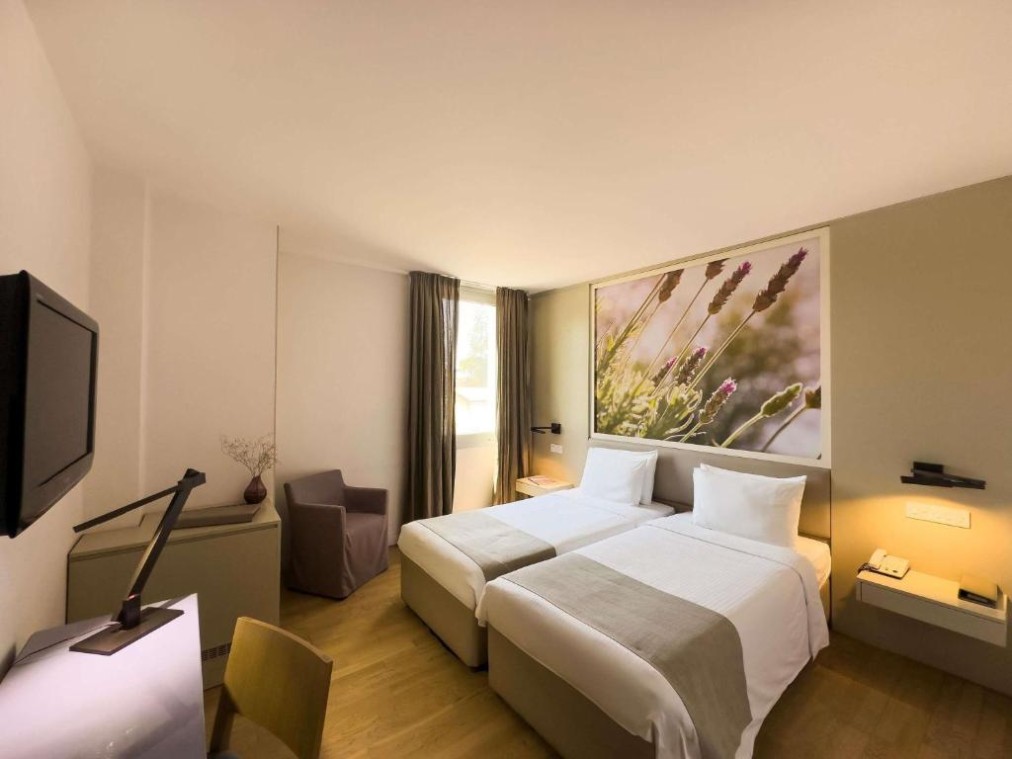 Gästezimmer mit zwei Betten, Schreibtisch, TV, Sessel und großem Blumenbild hinter den Betten.