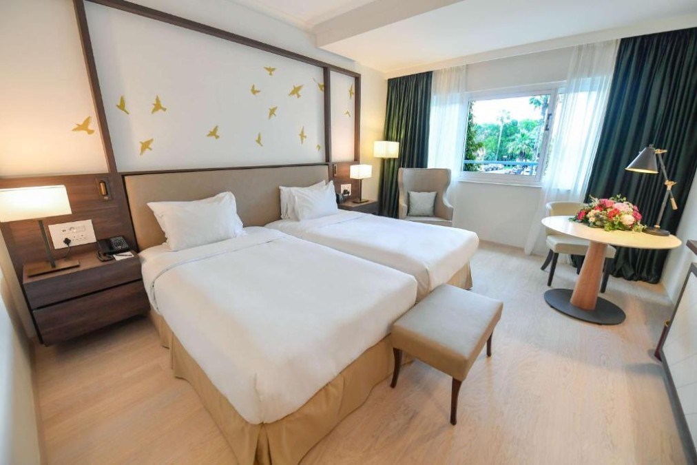 Zweibettzimmer mit Rundtisch, Blumen und Sitzplatz am Fenster.
