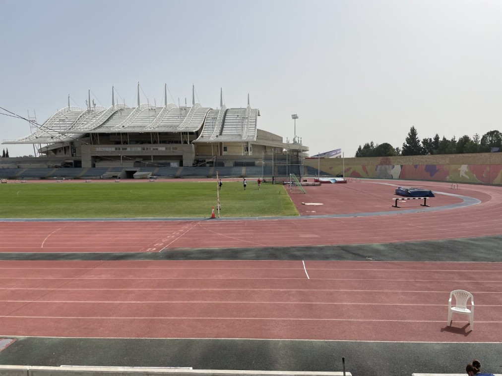 Stade d'athlétisme extérieur avec piste de course rouge, terrain vert et tribune moderne pour stages d'entraînement