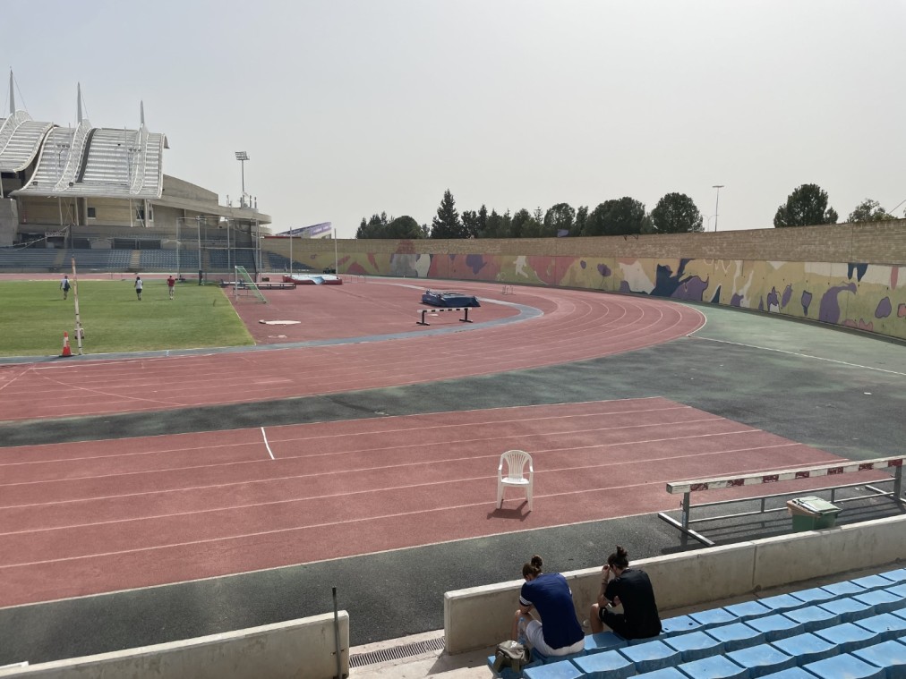 Installation d'athlétisme avec piste rouge incurvée, fresque murale colorée et athlètes se reposant sur les gradins bleus