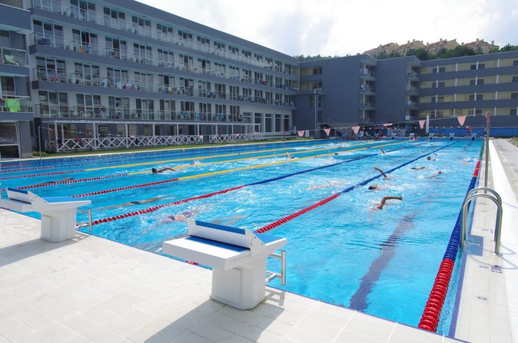 Piscine olympique extérieure à côté du bâtiment de l'hôtel avec nageurs s'entraînant pendant une séance de pratique